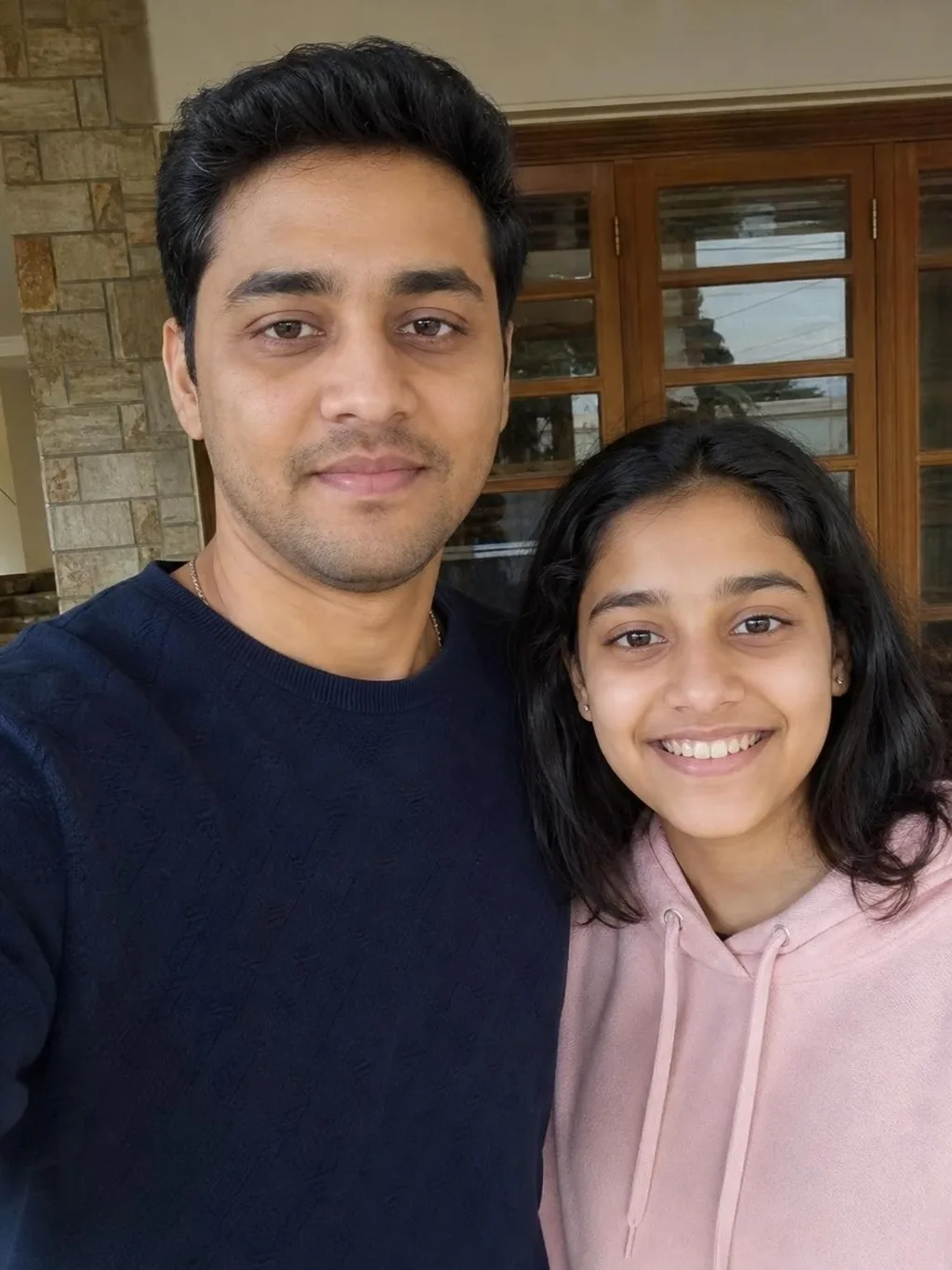 Input photo one: a selfie of a man in a navy sweater and a girl in a pink hoodie, taken outside a house
